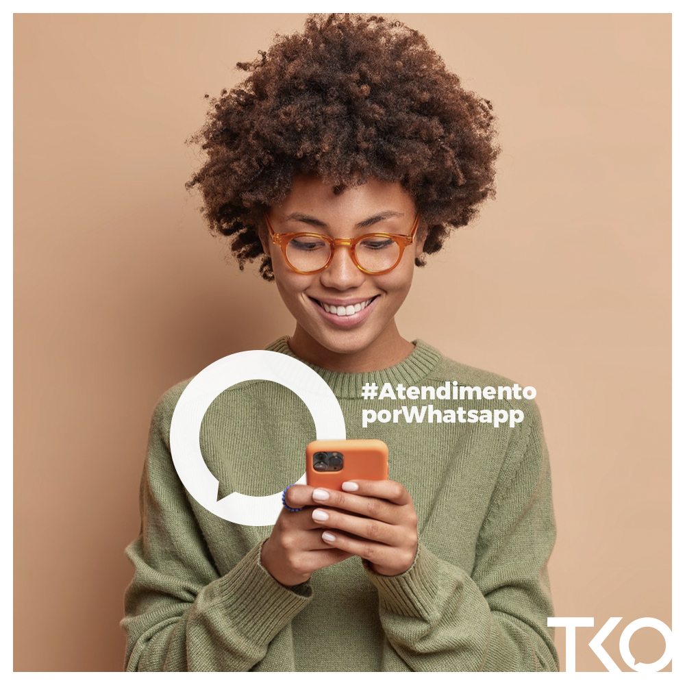 Mulher negra sorrindo e olhando para um celular que está segurando. Texto na imagem: "atendimento por WhatsApp." 